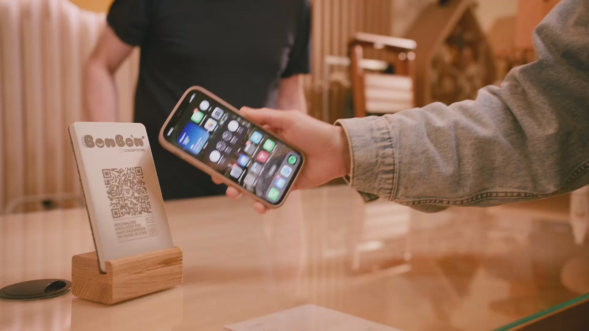 Kurze visuelle Impression, wie der Aufsteller funktioniert. Man sieht eine Kundin, die ihr Smartphone an den NFC Aufsteller von brique hält und sich ein Link öffnet.